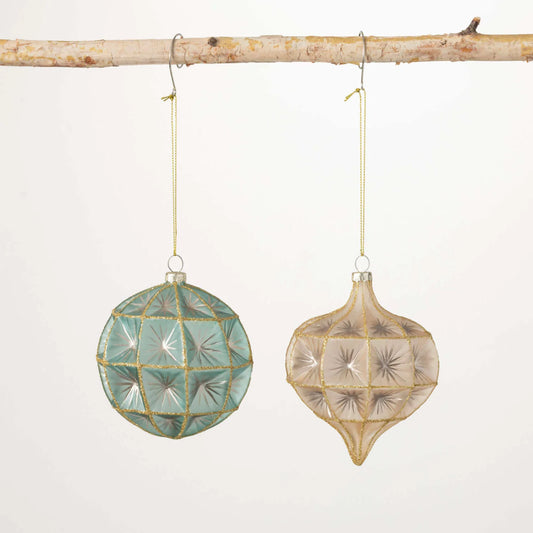 Two mercury glass ornaments hanging from strings, one is a geometric ball with a blue tint and the other is an onion-shaped with a beige tint, both decorated with metallic starburst patterns.