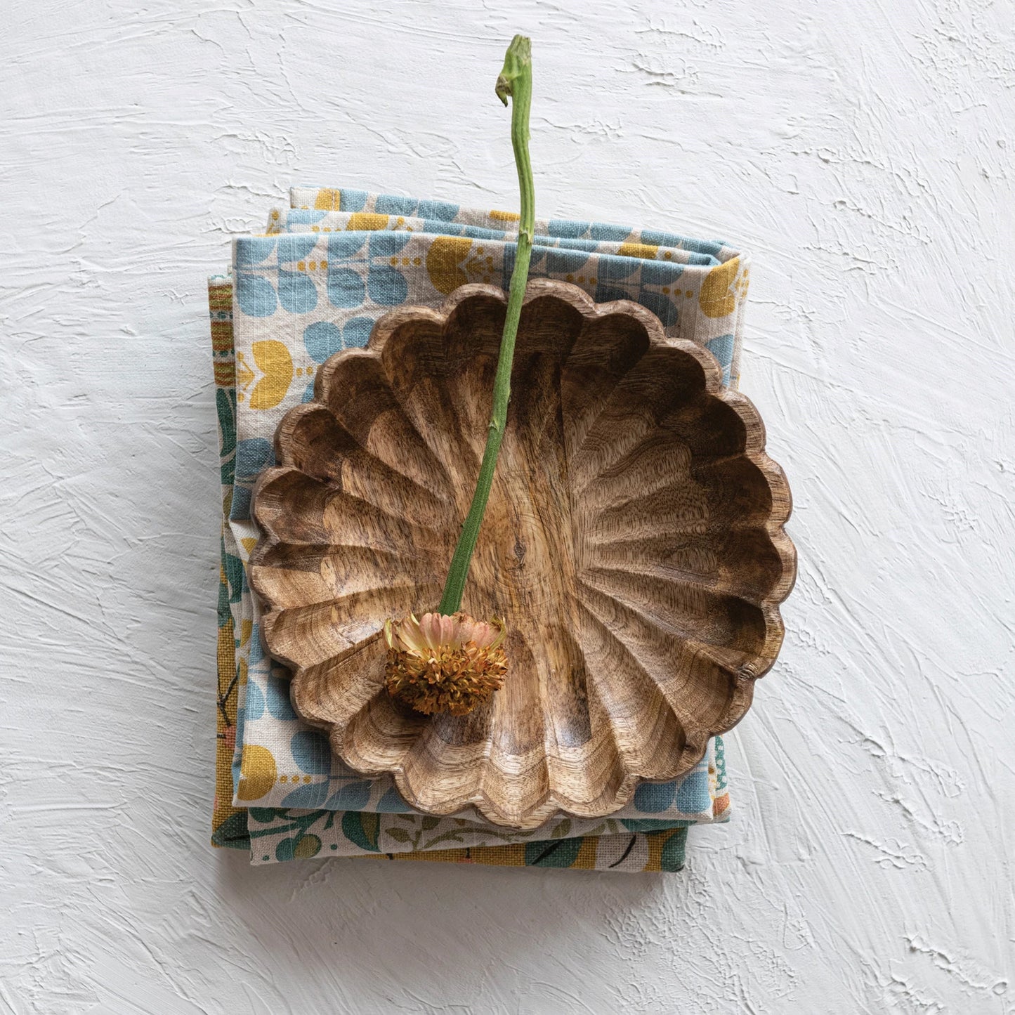 A scalloped edge mango wood bowl with a natural pattern, displayed on a patterned fabric.