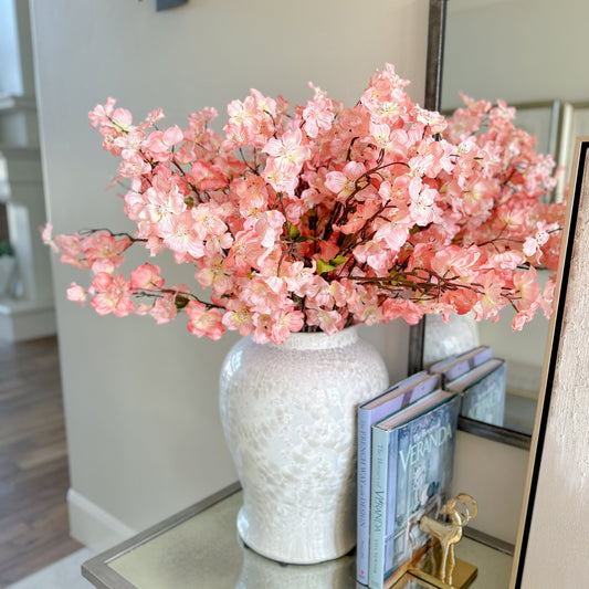 A 36 inch artificial Dogwood stem with peachy pink blossoms and a pearl accent, displayed in a white vase on a table.