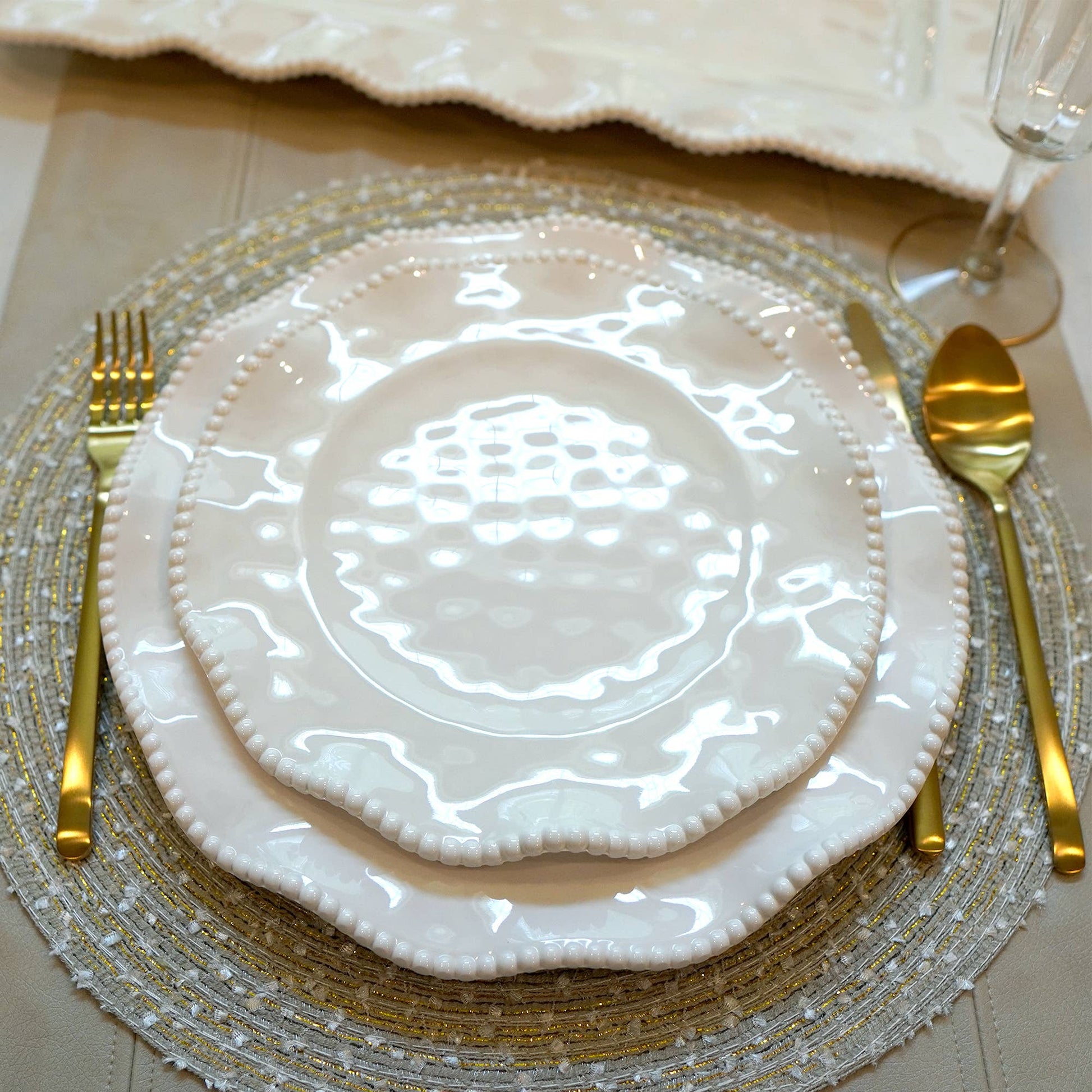 Elegant table setting with white melanine plates, gold cutlery, and a decorative placemat.