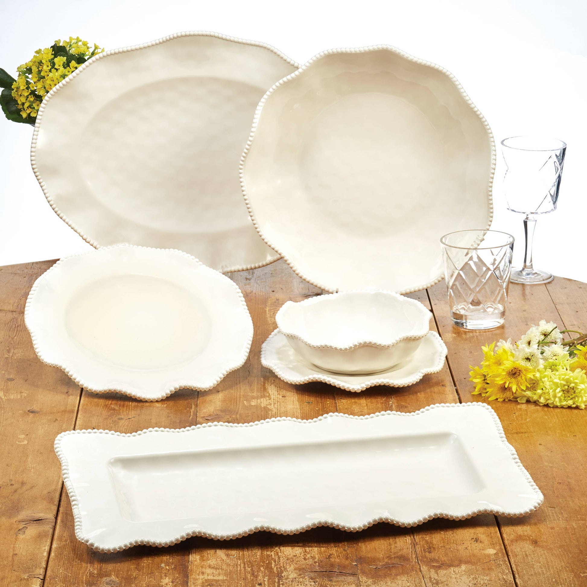 Set of white melamine dishes on a wooden table with yellow flowers.