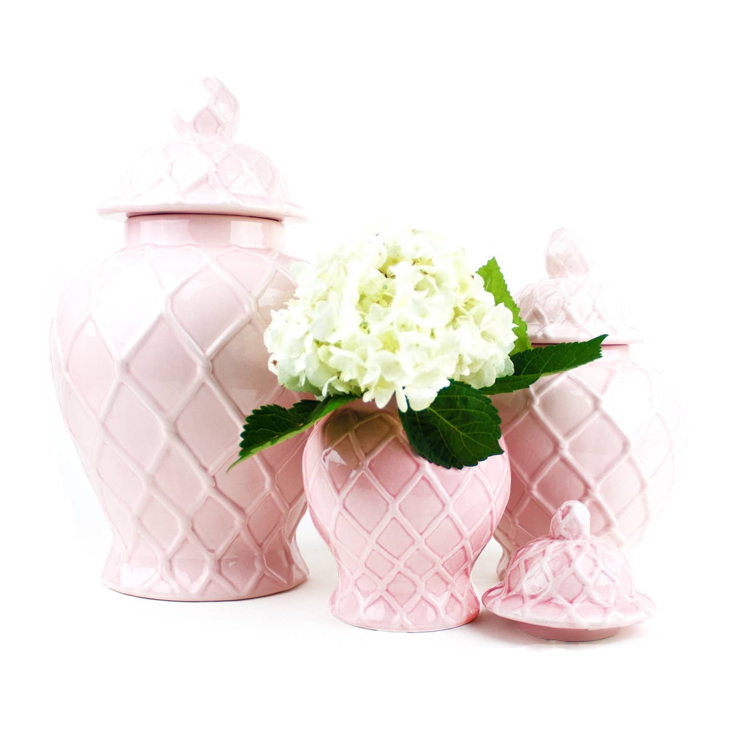 Set of pink ceramic jars with a diamond pattern, one holding white flowers on a white background.