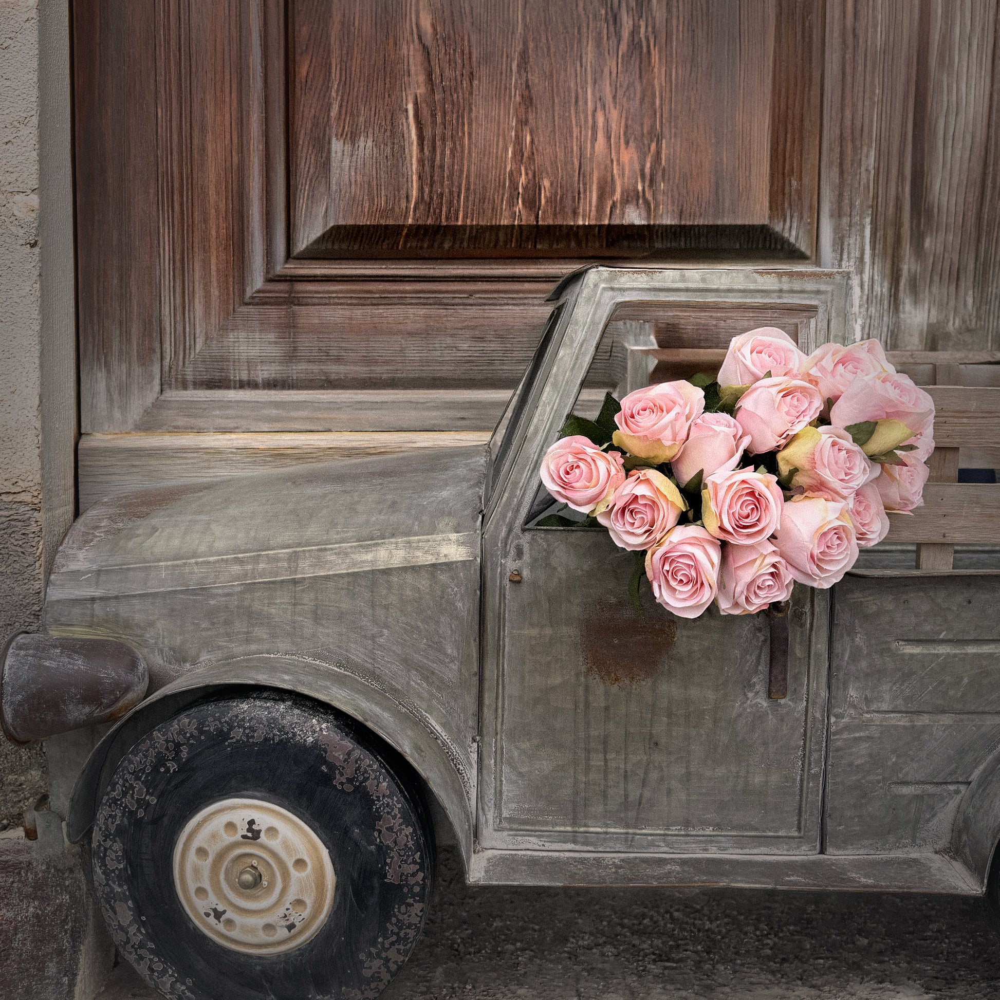 Small metal car with pink roses against a wooden door background