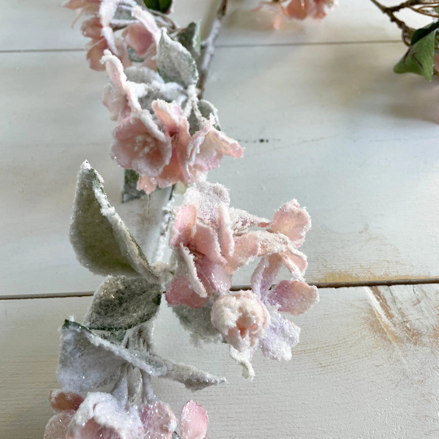 Decorative floral branch with pink flowers and green leaves on a wooden surface