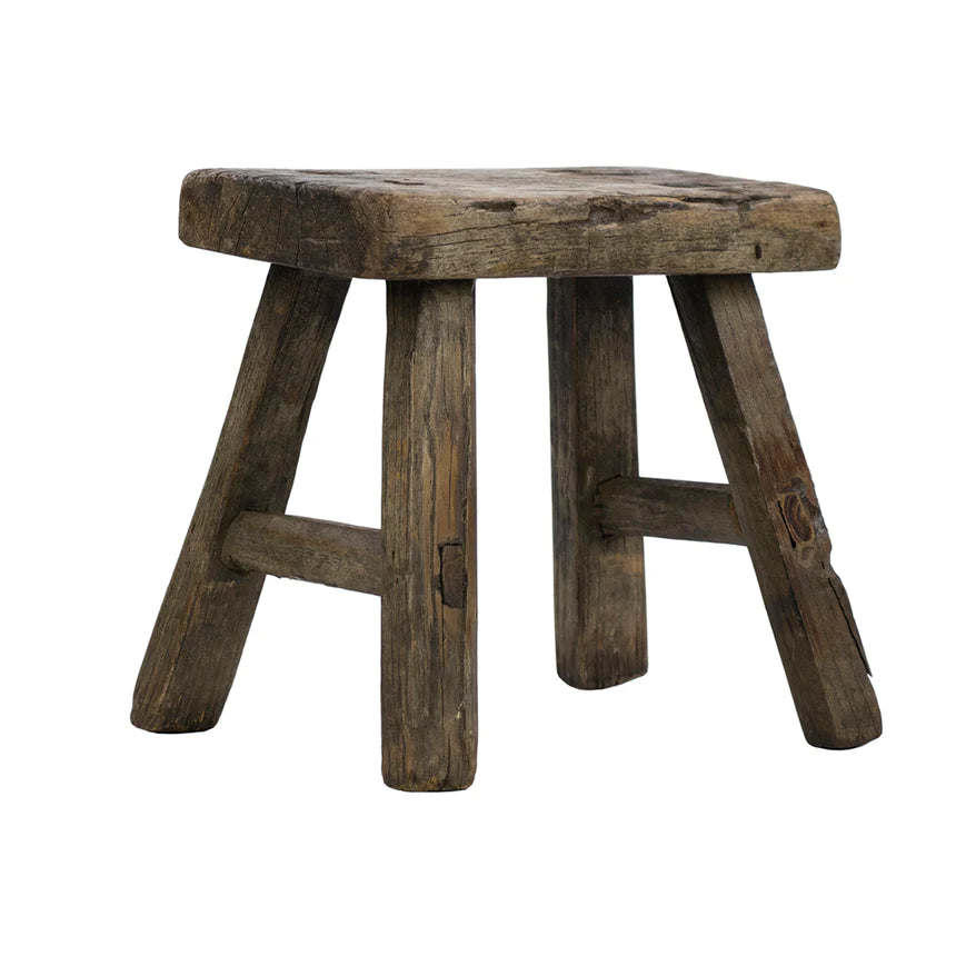 A rustic, reclaimed wood stool with a flat top and three legs.