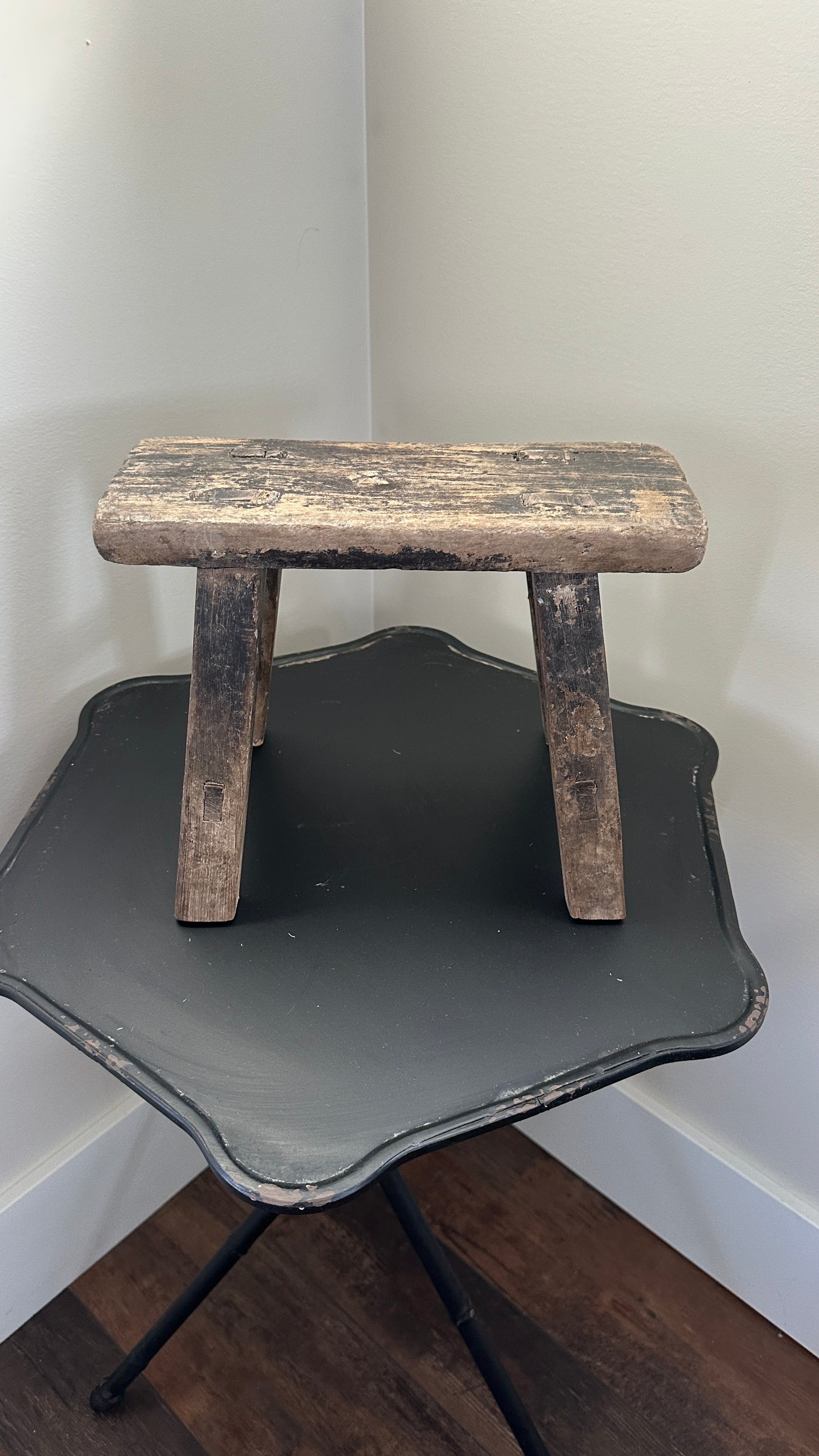 Wooden step stool with a black tray on a wooden floor against a white wall.