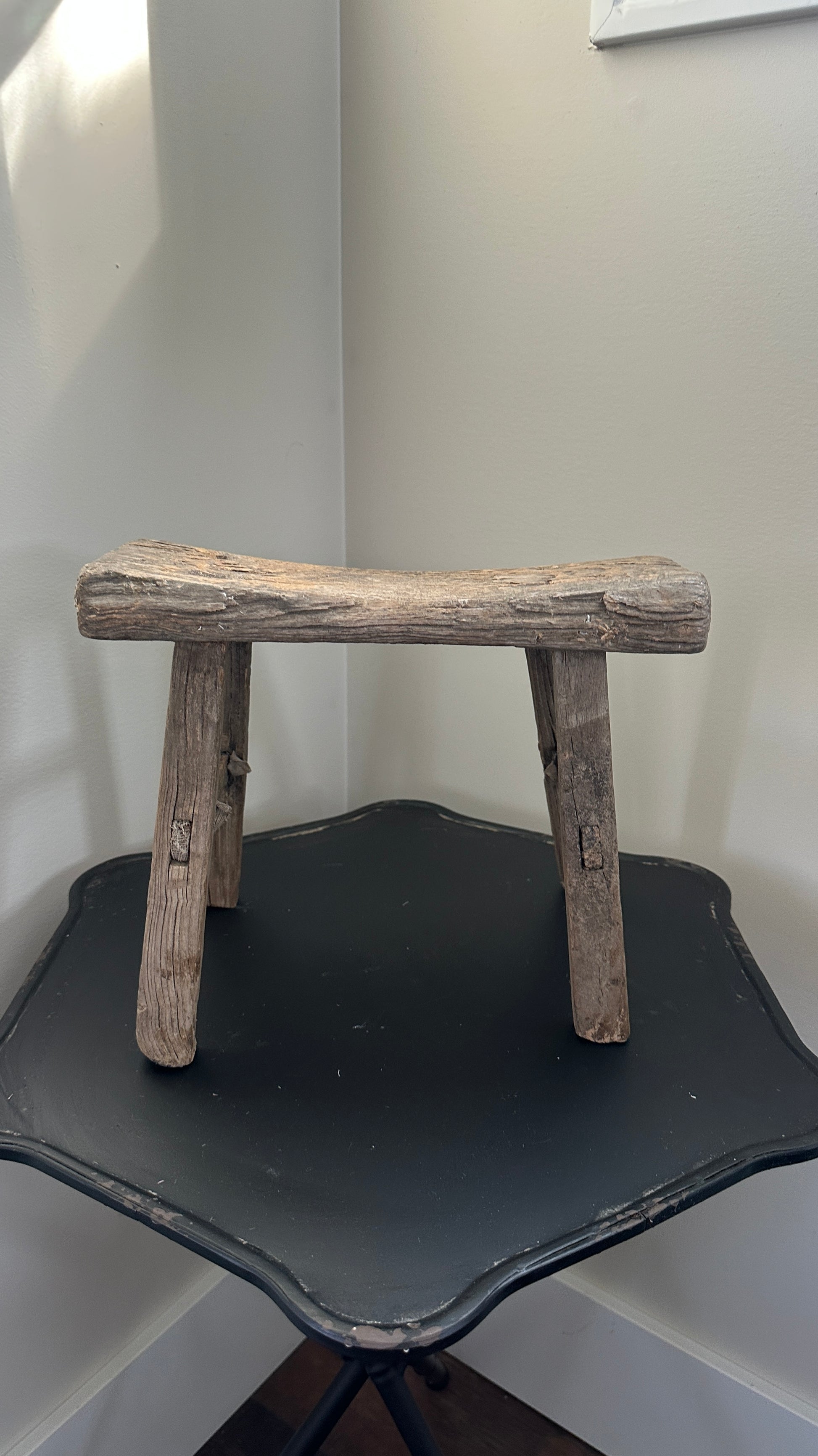 Wooden stool on a black surface against a light-colored wall