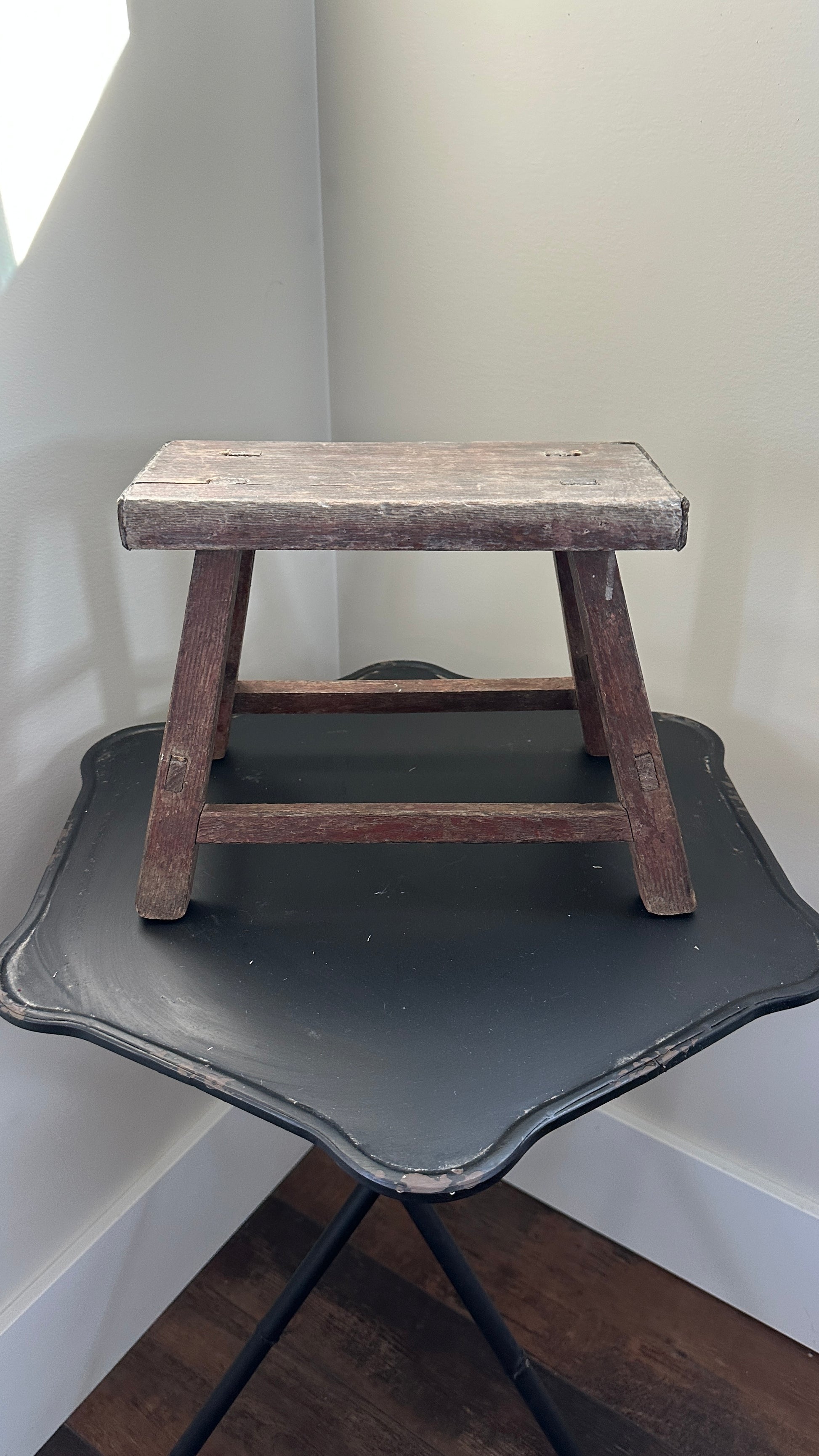 Wooden step stool on a black metal stand against a white wall.