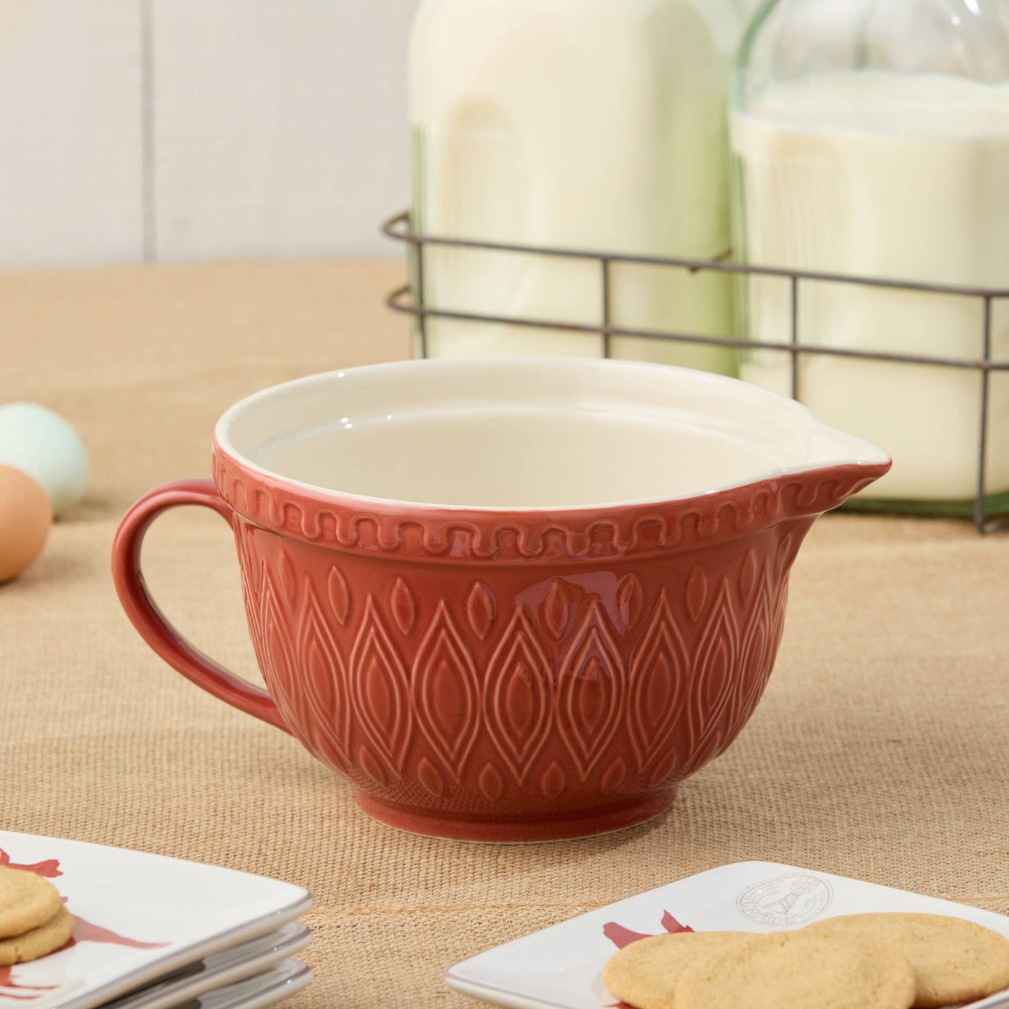 Red 2.5 quart mixing bowl with decorative patterns on a table with cookies and eggs.