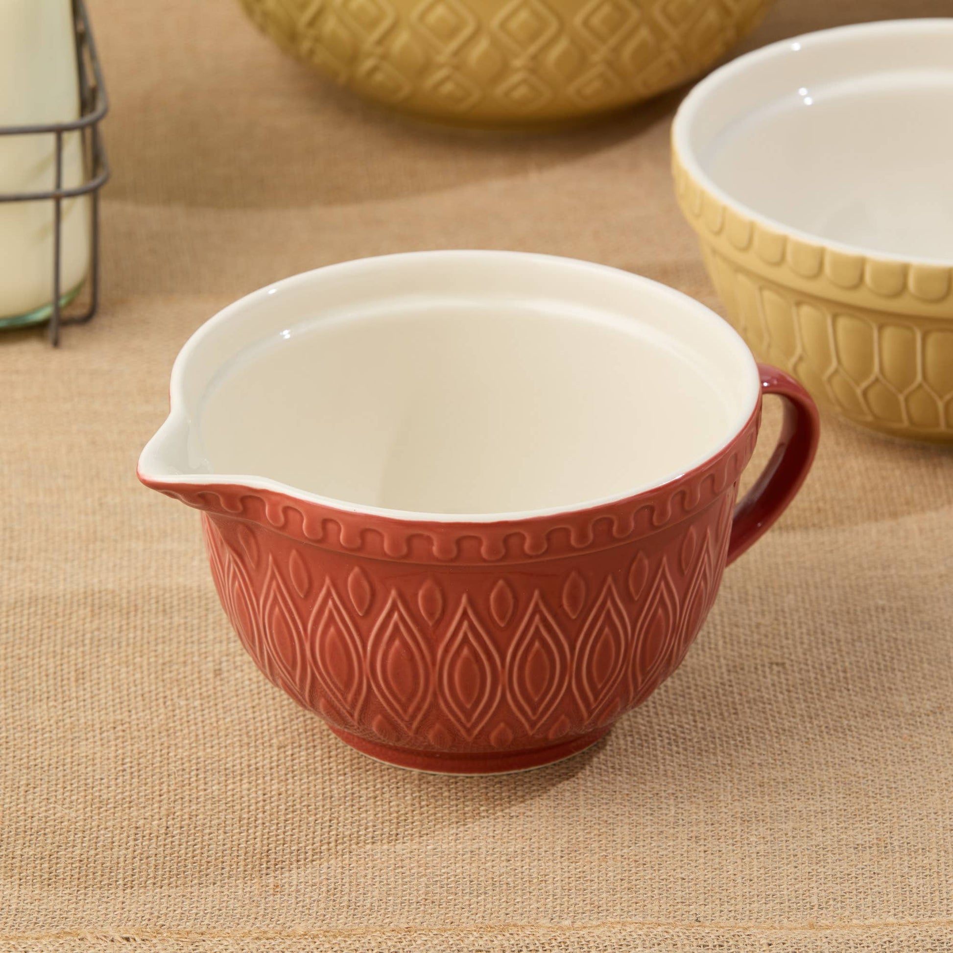 Red ceramic 2.5 quart mixing bowl with white interior on a beige surface