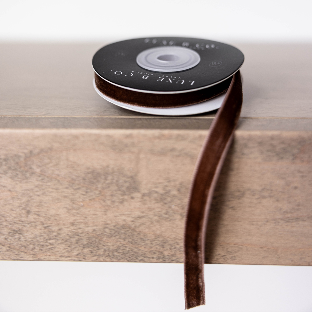 Spool of brown ribbon on a wooden surface with a white background