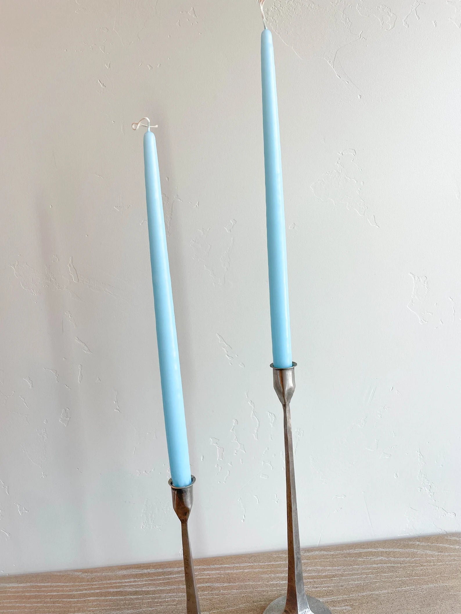 Two robin egg blue hand-dipped tapered candles with metal sticks, placed on a surface against a plain background.
