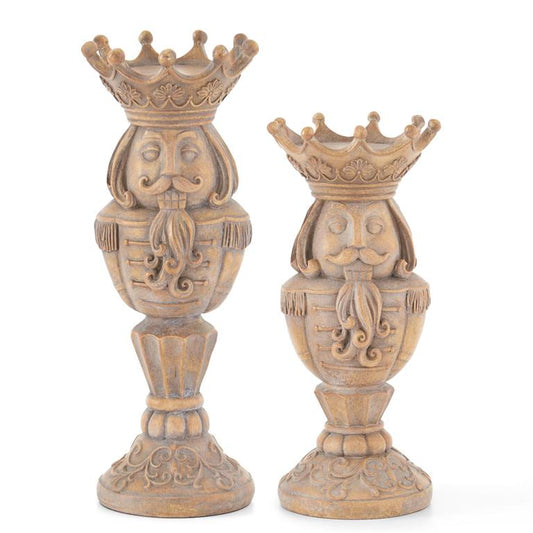 Two gray washed brown resin nutcracker candle holders with ornate designs and crown-like tops.