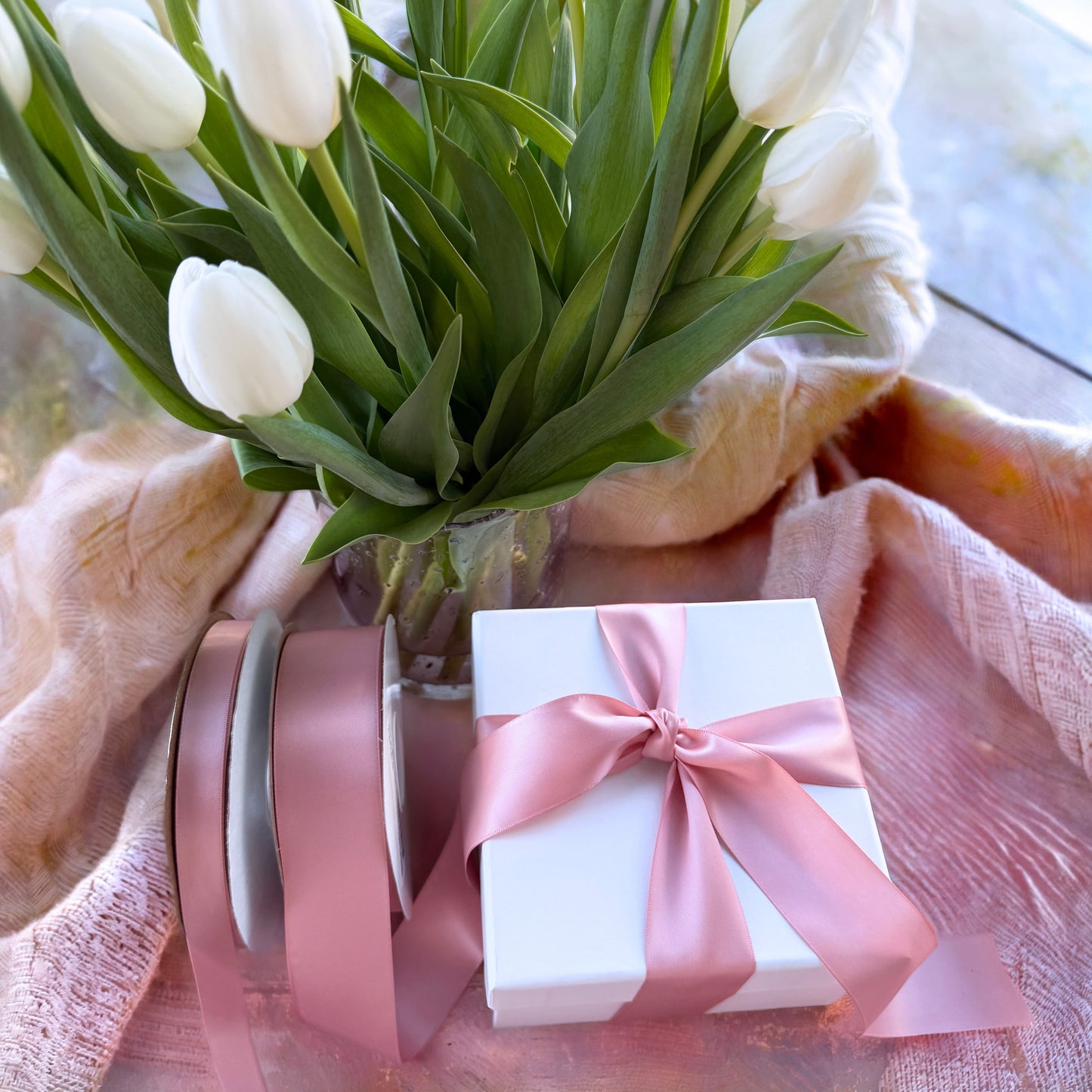 A gift box featuring a pink ribbon on a soft fabric background.