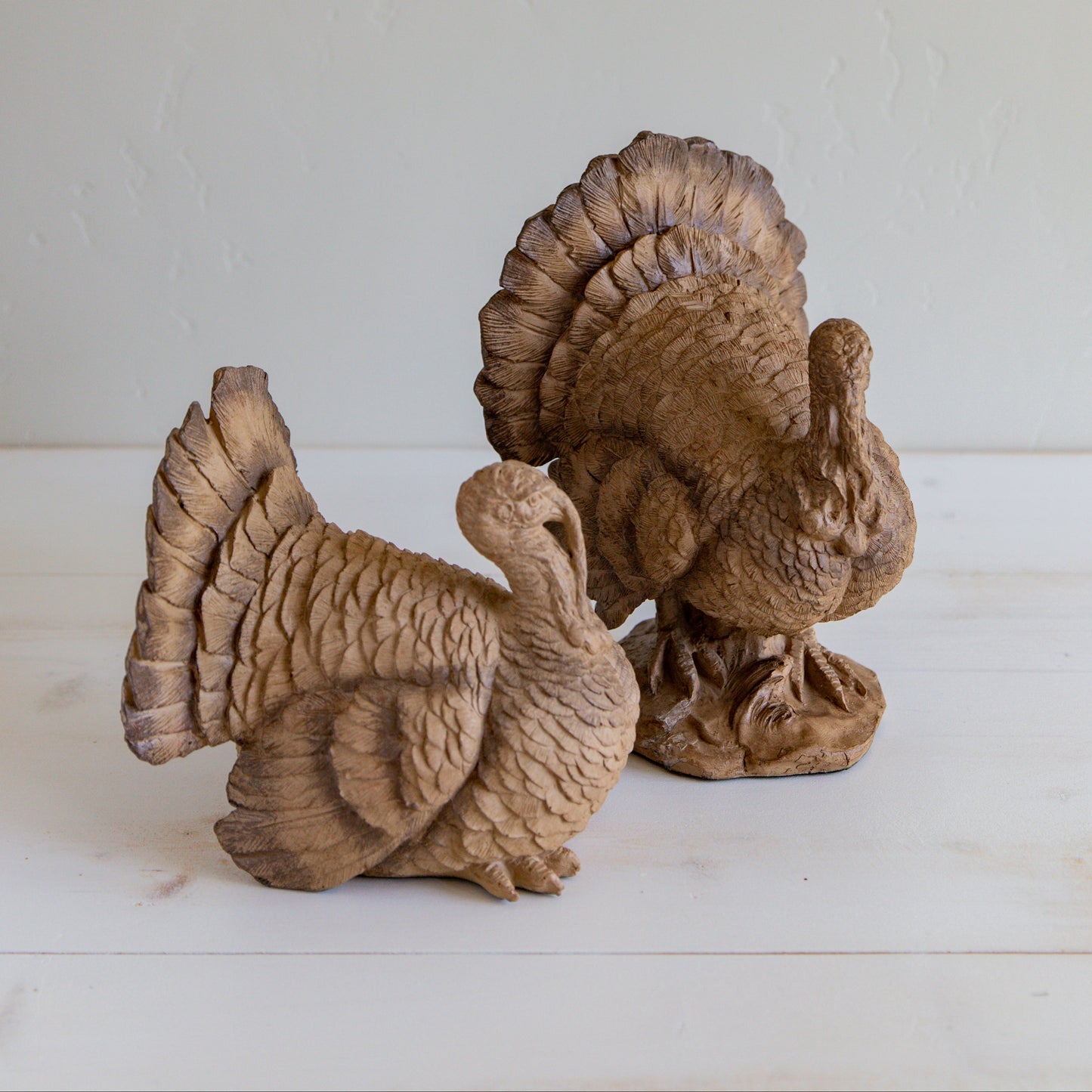 Two brown resin standing turkey figurines placed on a wooden surface against a white wall.