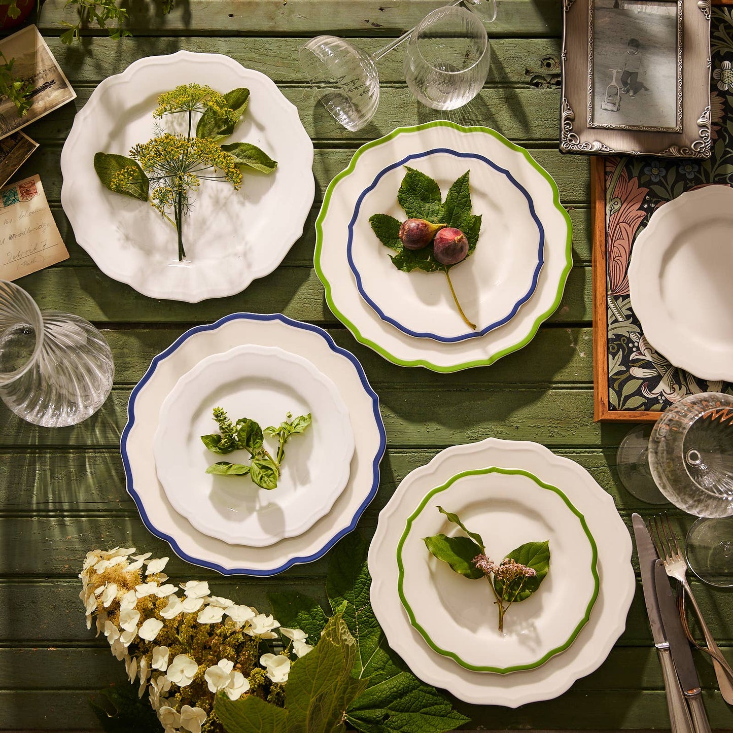 White plates with green and blue accents on a wooden table with flowers and cutlery.
