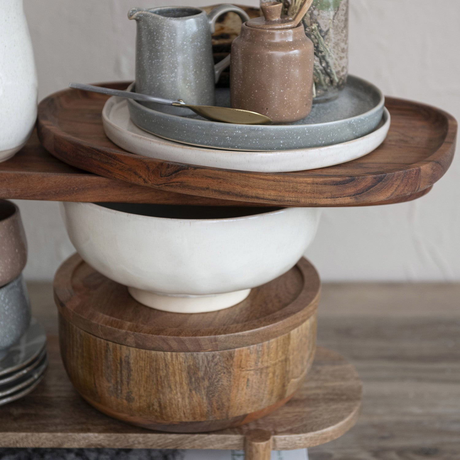 Wooden tiered stand with ceramic bowls and a teapot on a neutral background