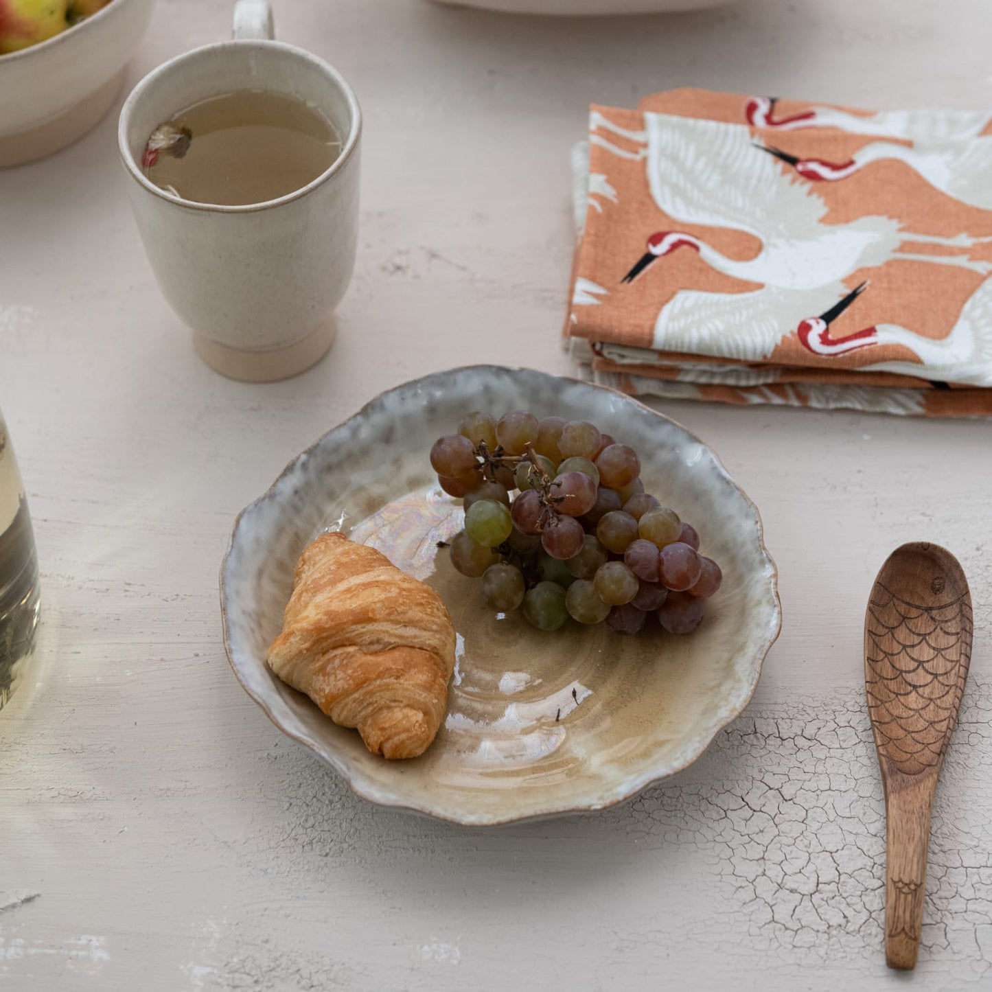 Bowl with a croissant and grapes on a table with a mug and napkins.