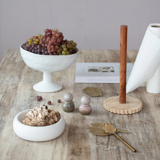 A white stoneware footed bowl with a reactive crackle glaze is displayed on a wooden table. 