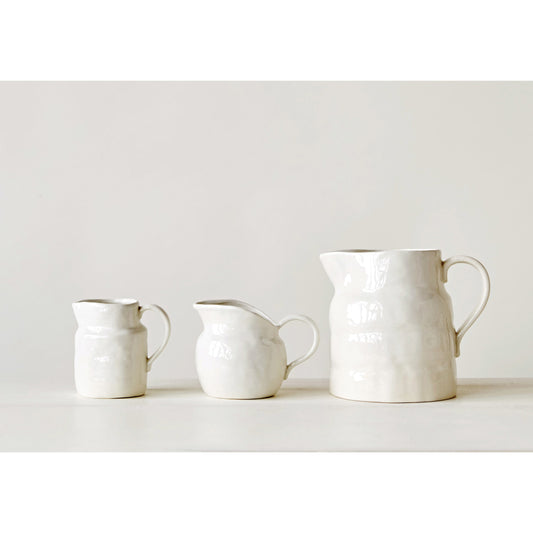 A set of three white stoneware pitchers in varying sizes displayed on a neutral background.