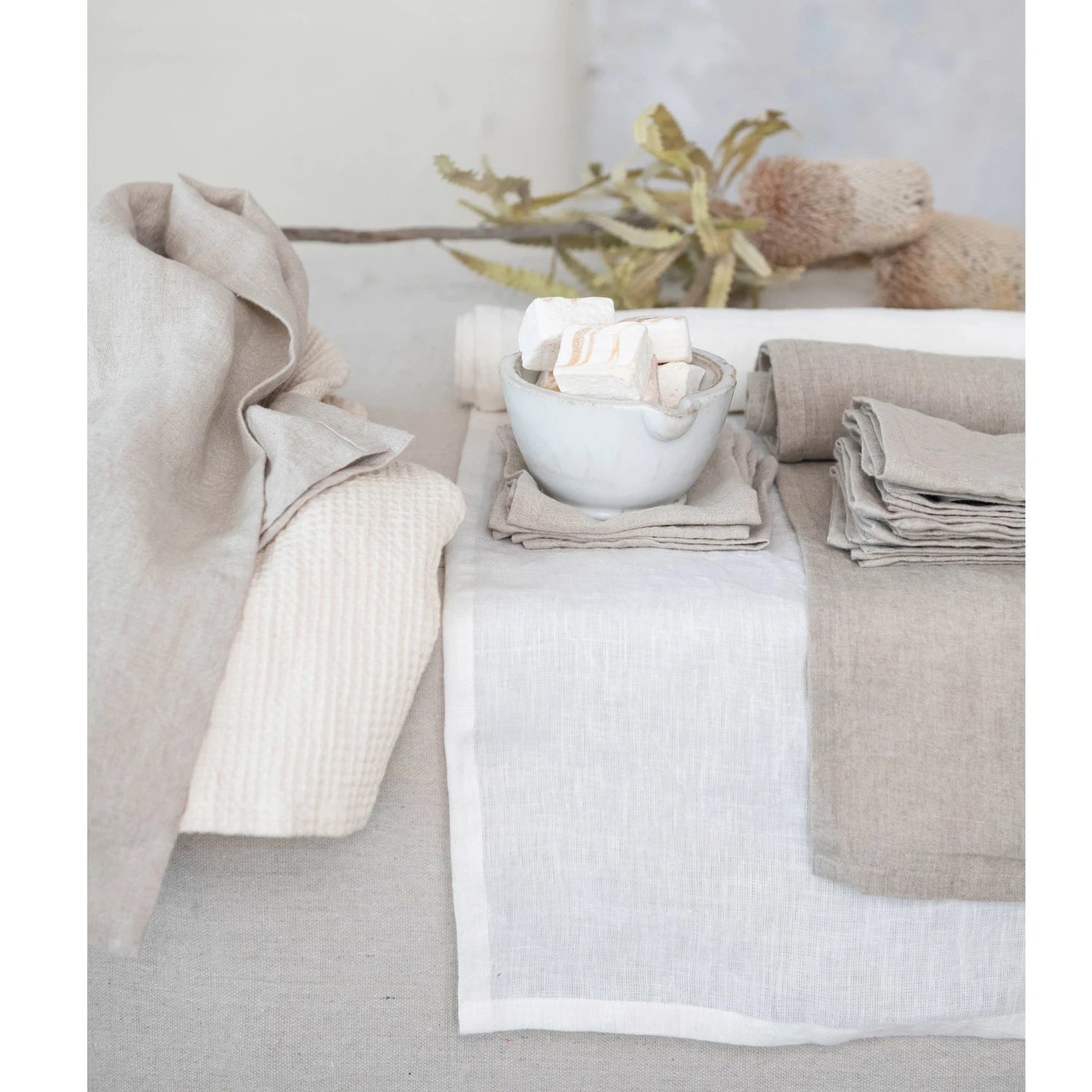 A beige linen table runner displayed on a table setting, with a stonewashed texture visible.