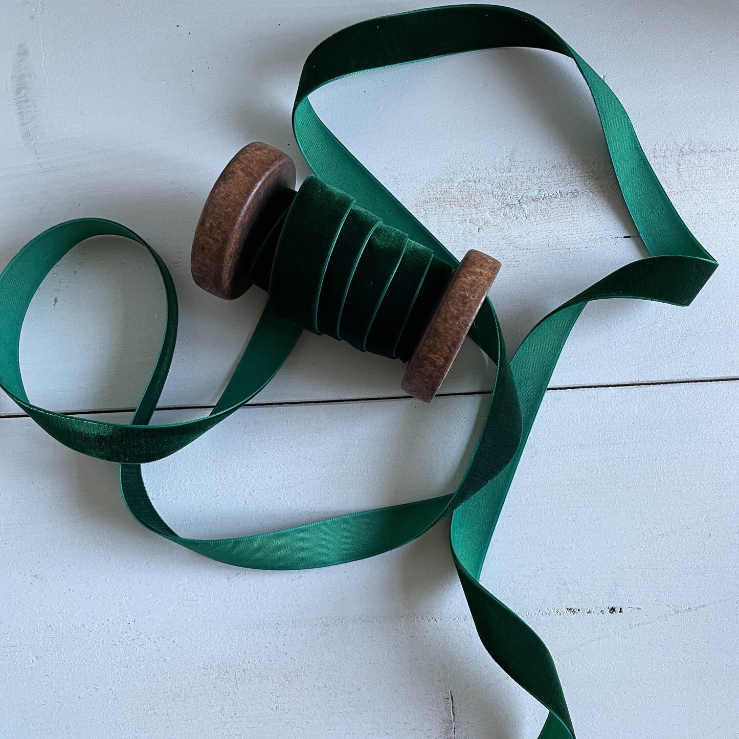 A green velvet ribbon with a woven edge, displayed alongside its spool on a wooden surface.