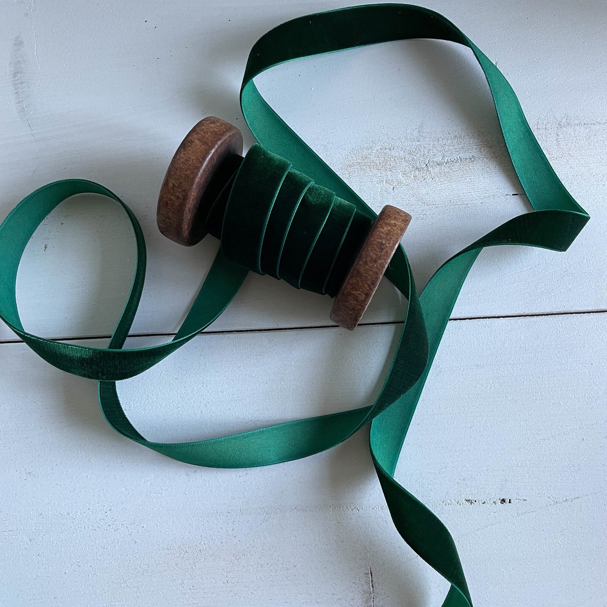 A green velvet ribbon with a woven edge, displayed alongside its spool on a wooden surface.