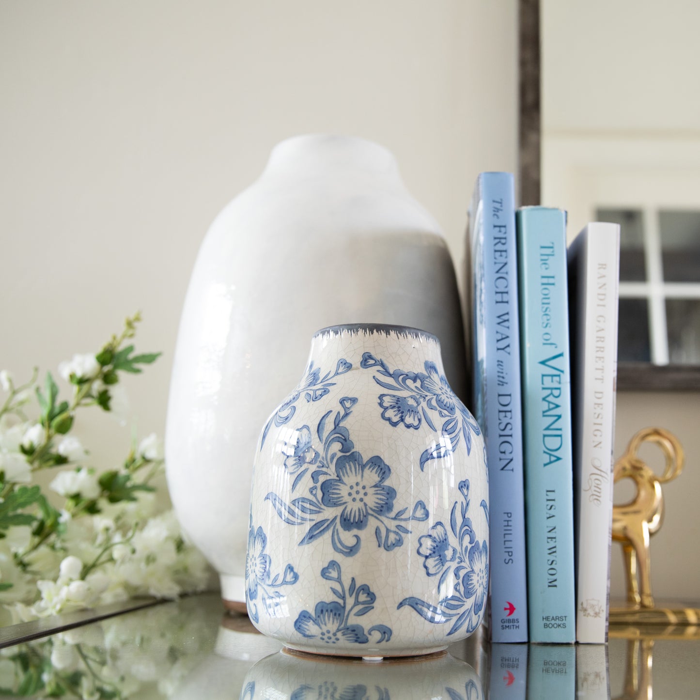 Decorative white vase with blue floral patterns on a surface with books and flowers.