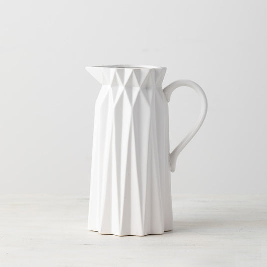 A white ceramic origami-inspired pitcher with a geometric pattern.