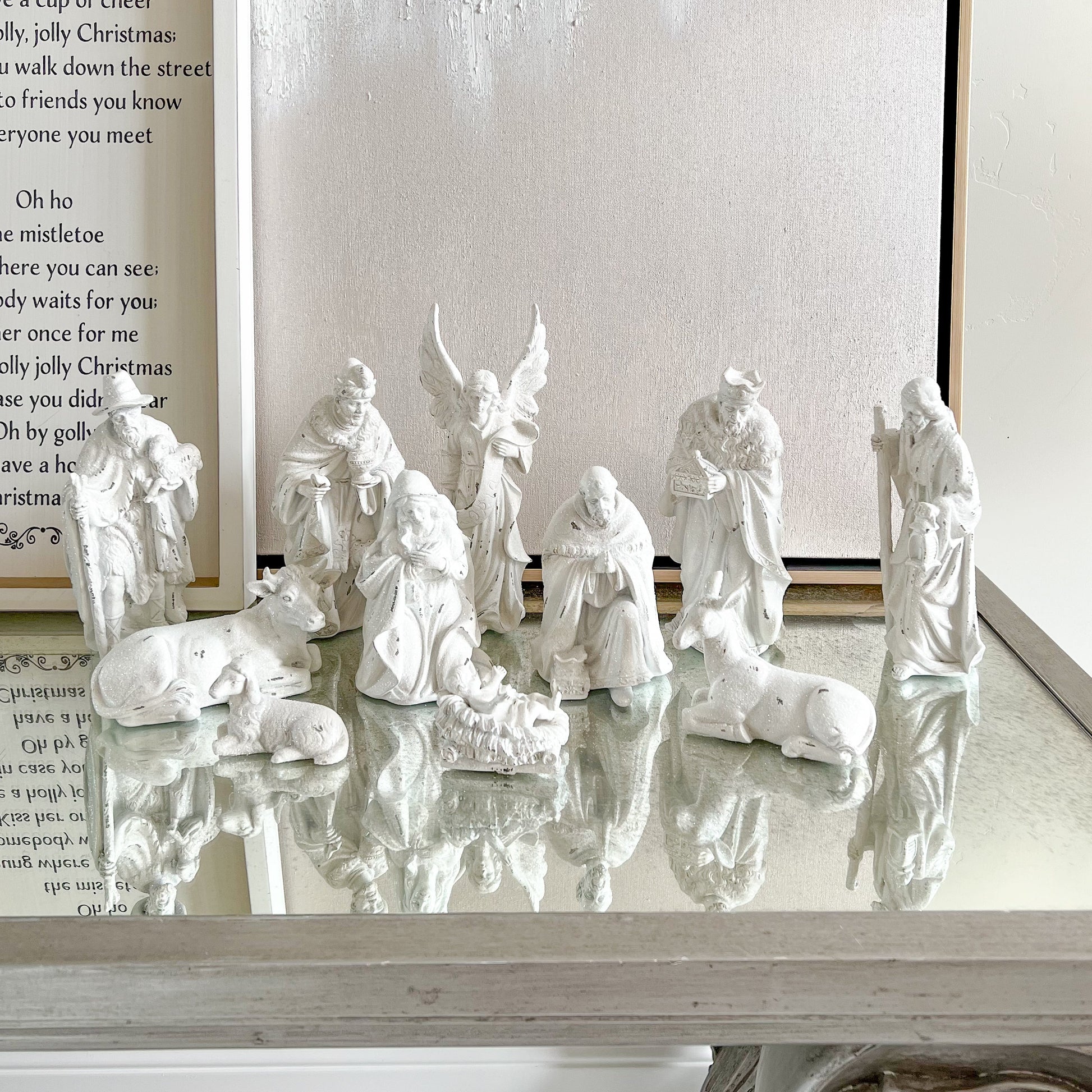 White nativity scene on a reflective surface with a framed text in the background