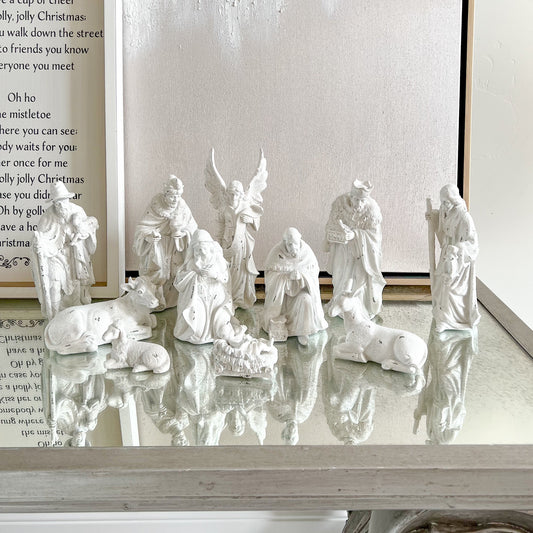 White nativity scene on a reflective surface with a framed text in the background