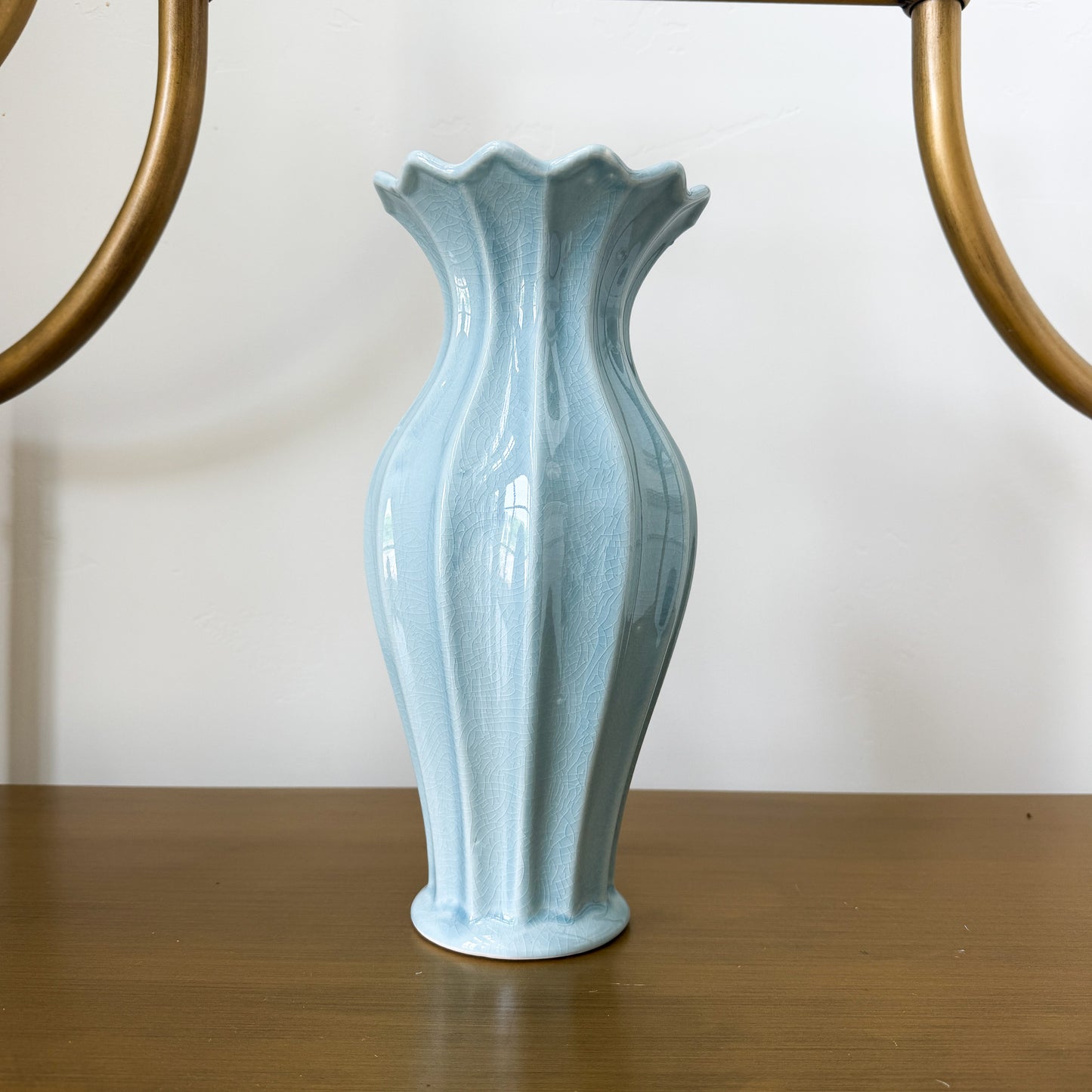 Light blue ceramic vase on a wooden surface with a white wall background