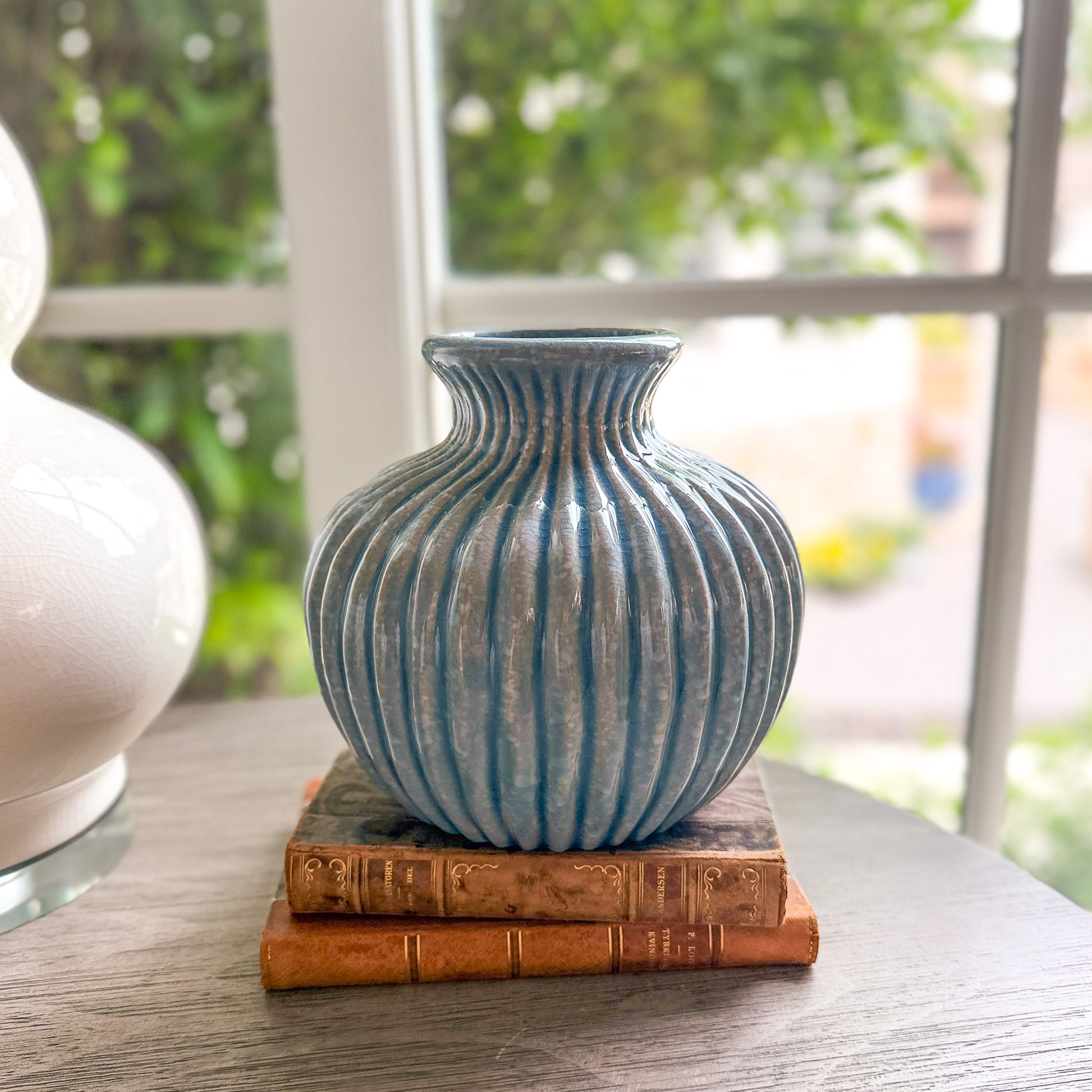 Blue ribbed vase on two books with a blurred outdoor background