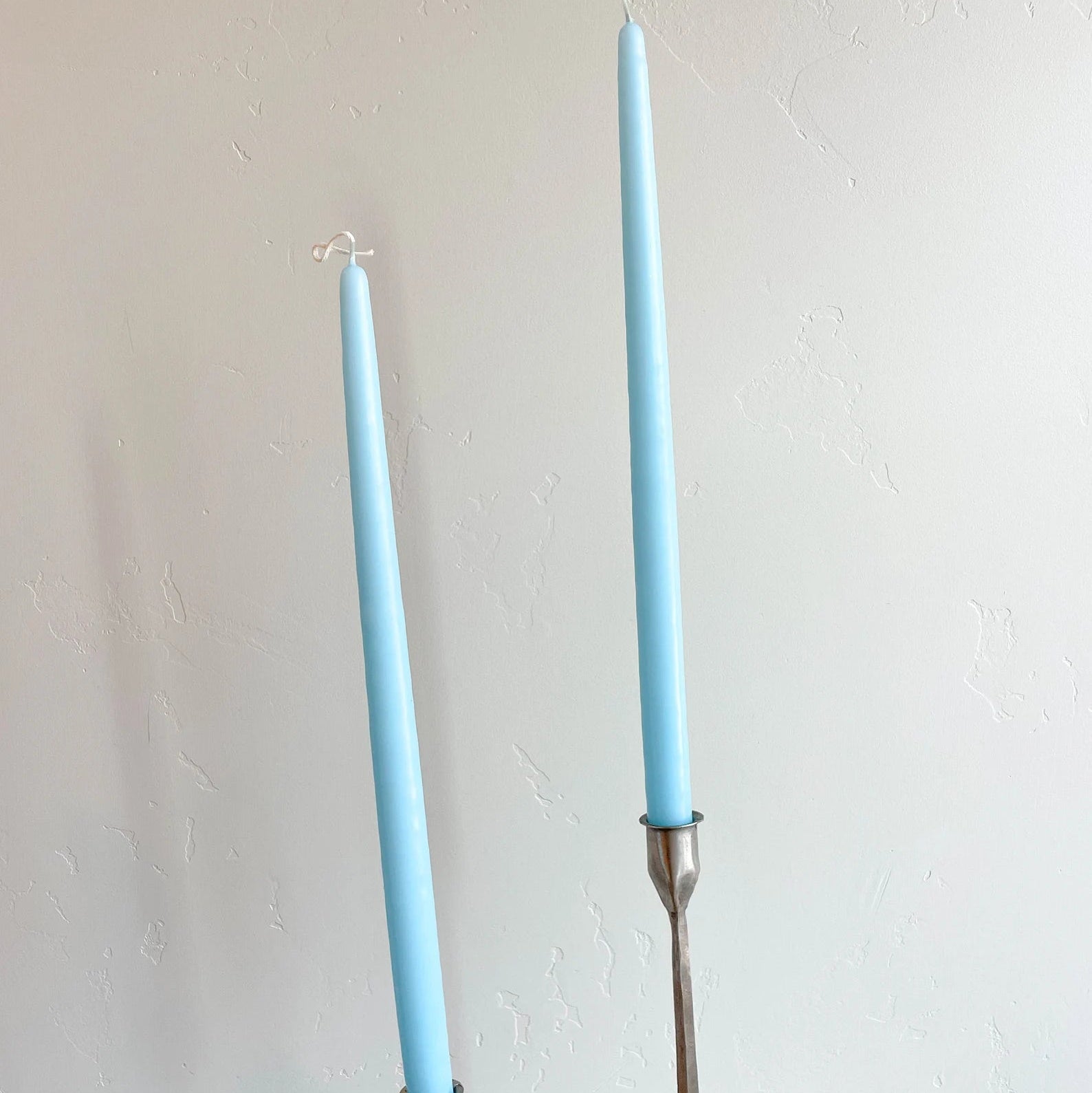 Two robin egg blue hand-dipped tapered candles with metal sticks, placed on a surface against a plain background.