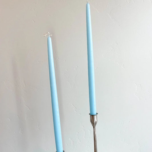 Two robin egg blue hand-dipped tapered candles with metal sticks, placed on a surface against a plain background.